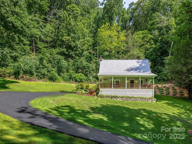 view of front of property with a porch, a chimney, a front yard, and a wooded view