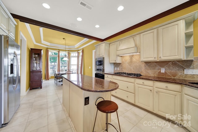 kitchen with backsplash, appliances with stainless steel finishes, cream cabinetry, and custom range hood