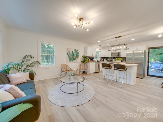 living room with light wood-type flooring, a notable chandelier, and ornamental molding