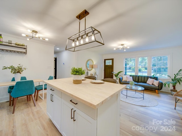 kitchen featuring decorative light fixtures, light hardwood / wood-style flooring, ornamental molding, white cabinets, and a center island