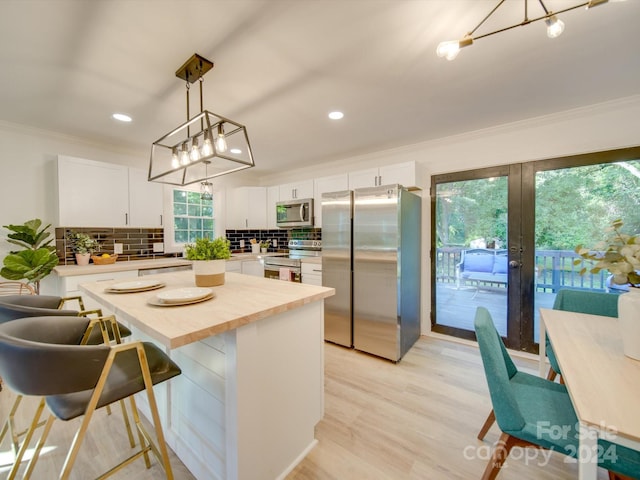 kitchen featuring appliances with stainless steel finishes, backsplash, white cabinetry, light wood-type flooring, and a kitchen island