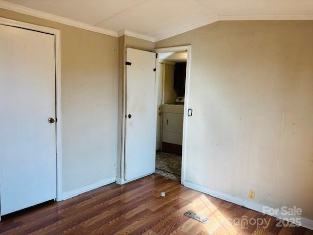 unfurnished bedroom with washer / dryer, lofted ceiling, crown molding, dark wood-type flooring, and a closet