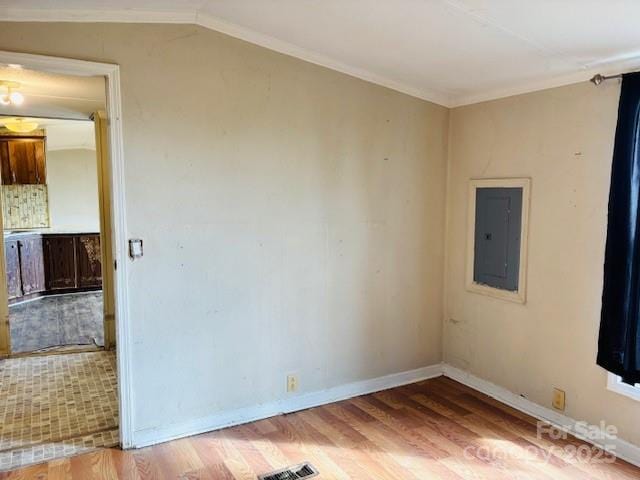 empty room featuring crown molding, wood-type flooring, electric panel, and vaulted ceiling