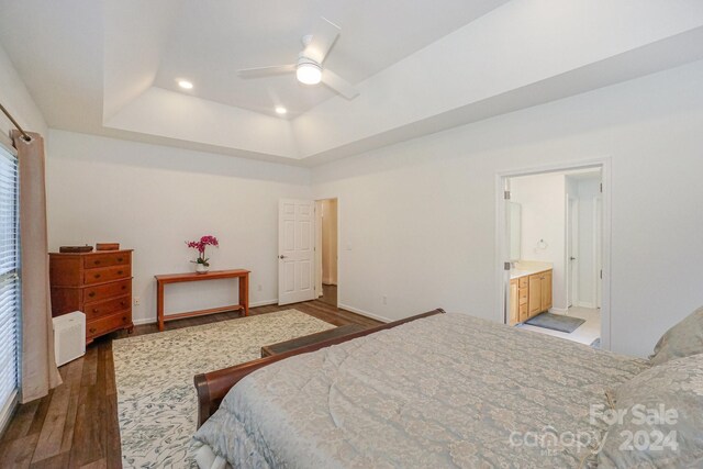 bedroom featuring ceiling fan, a tray ceiling, connected bathroom, and dark hardwood / wood-style flooring