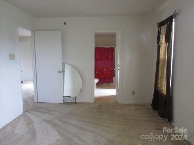 unfurnished bedroom featuring light colored carpet and connected bathroom