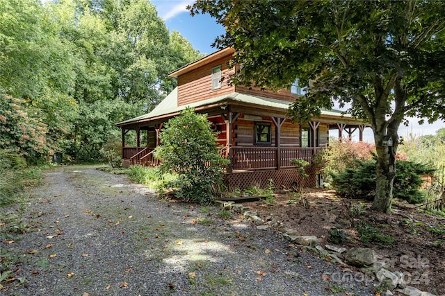 view of side of home featuring gravel driveway, metal roof, and a porch