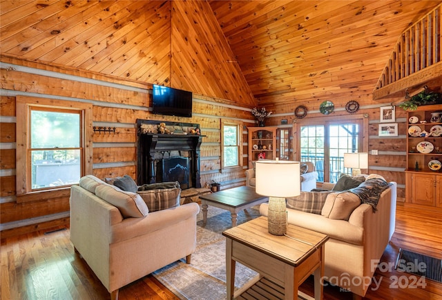 living area with wooden walls, high vaulted ceiling, a fireplace with raised hearth, and wood finished floors