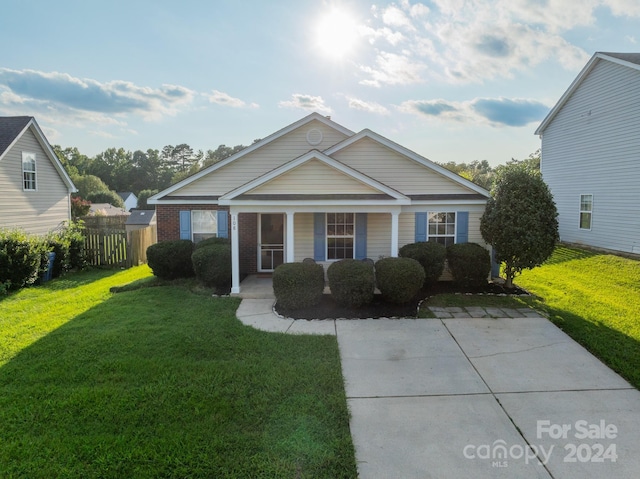 bungalow featuring covered porch, brick siding, fence, and a front lawn