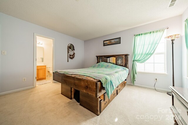 bedroom with a textured ceiling, light carpet, and ensuite bathroom