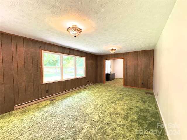 carpeted spare room with a baseboard heating unit, wood walls, a textured ceiling, and baseboards