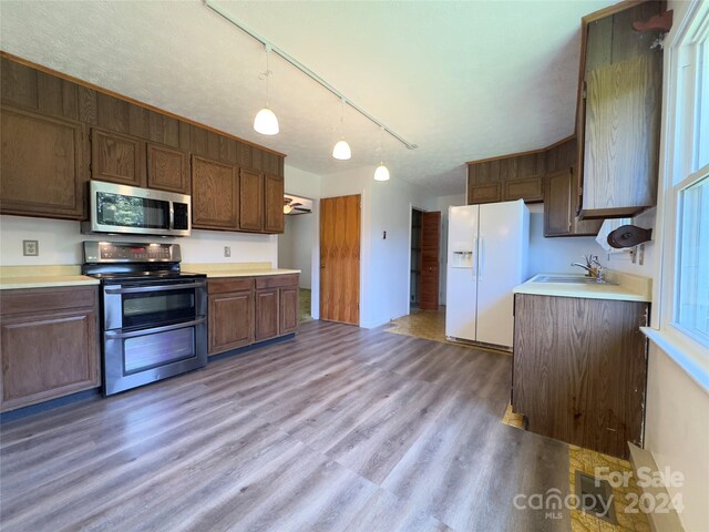 kitchen with track lighting, decorative light fixtures, stainless steel appliances, wood-type flooring, and sink