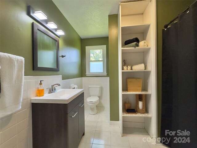 bathroom featuring tile patterned flooring, vanity, toilet, and tile walls