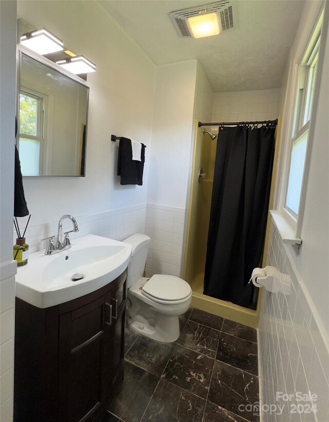 bathroom with tile walls, toilet, walk in shower, and vanity