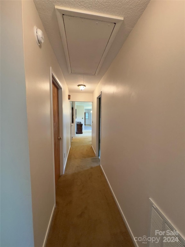 hall featuring visible vents, a textured ceiling, carpet flooring, and attic access