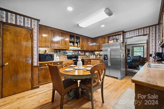 kitchen with a textured ceiling, black appliances, light hardwood / wood-style floors, and ornamental molding