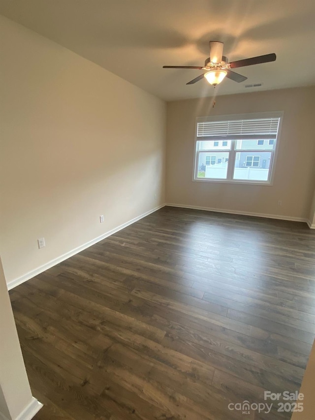 empty room featuring dark wood-style flooring, visible vents, and baseboards