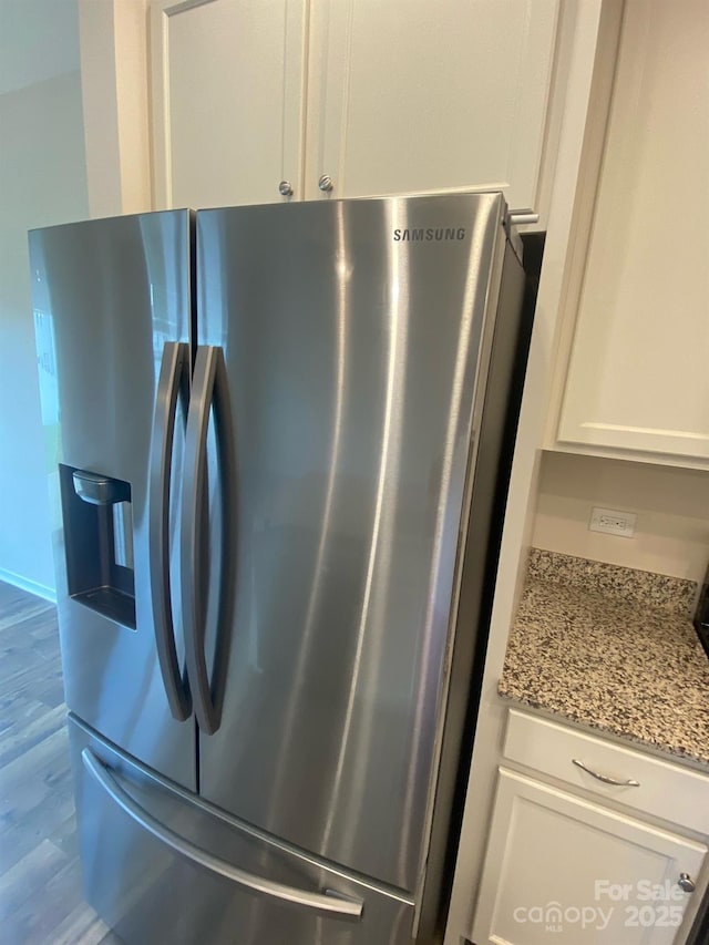 details featuring light stone countertops, stainless steel fridge, white cabinets, and wood finished floors