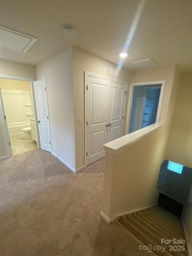 hallway featuring baseboards, visible vents, attic access, and light colored carpet