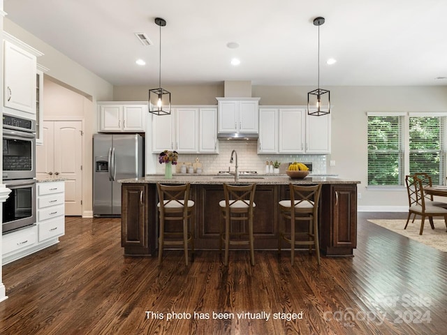 kitchen with appliances with stainless steel finishes, dark hardwood / wood-style floors, tasteful backsplash, a center island with sink, and white cabinets