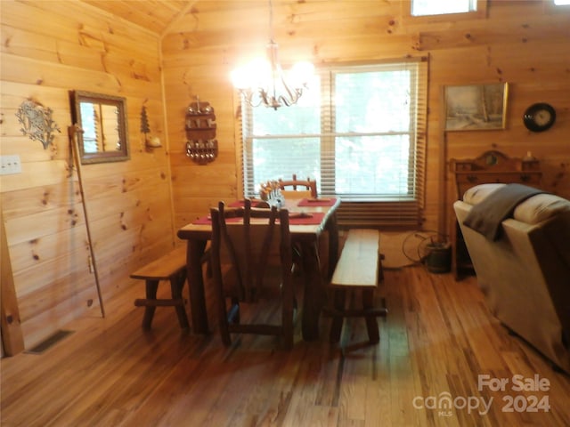 dining area with wooden walls, lofted ceiling, an inviting chandelier, and wood-type flooring