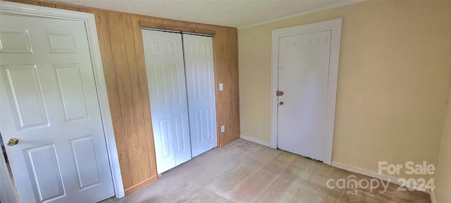 unfurnished bedroom featuring a closet, light colored carpet, wood walls, and baseboards