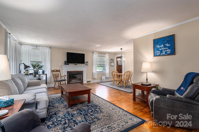 living room featuring ornamental molding, a glass covered fireplace, a textured ceiling, and wood finished floors