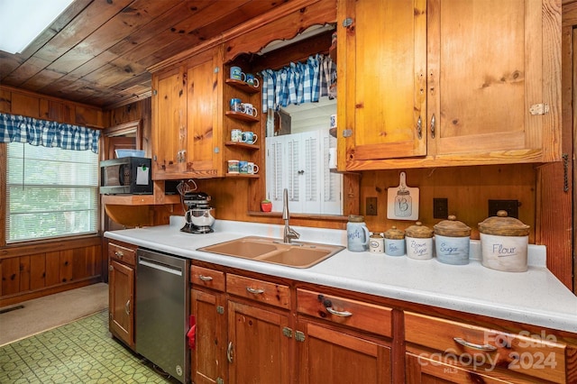 kitchen with light countertops, stainless steel dishwasher, a sink, and wooden walls