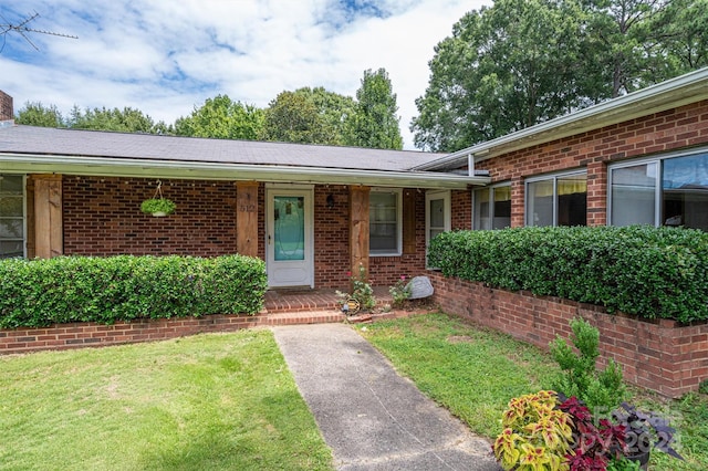 property entrance with covered porch, brick siding, and a lawn