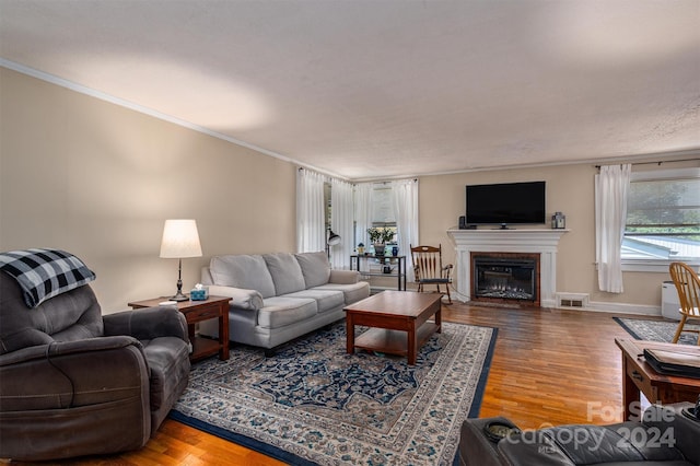 living room with ornamental molding, a glass covered fireplace, visible vents, and wood finished floors