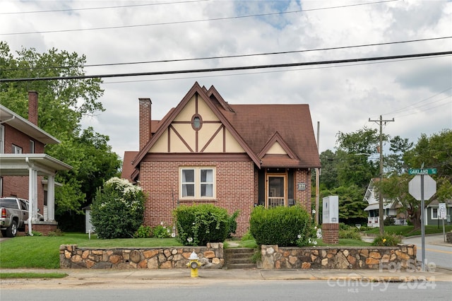 english style home featuring brick siding, a chimney, and stucco siding