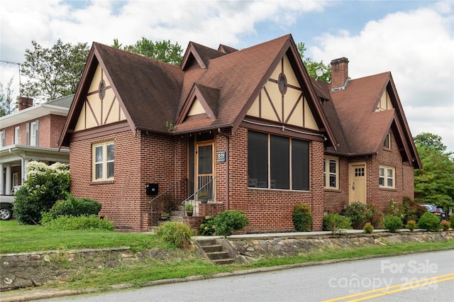 tudor home with stucco siding, a shingled roof, a chimney, and brick siding