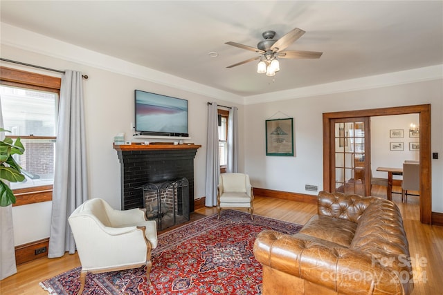 living room with a healthy amount of sunlight, ceiling fan, light hardwood / wood-style flooring, and a brick fireplace