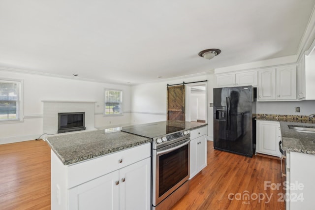 kitchen with a barn door, black fridge with ice dispenser, white cabinetry, and stainless steel range with electric cooktop