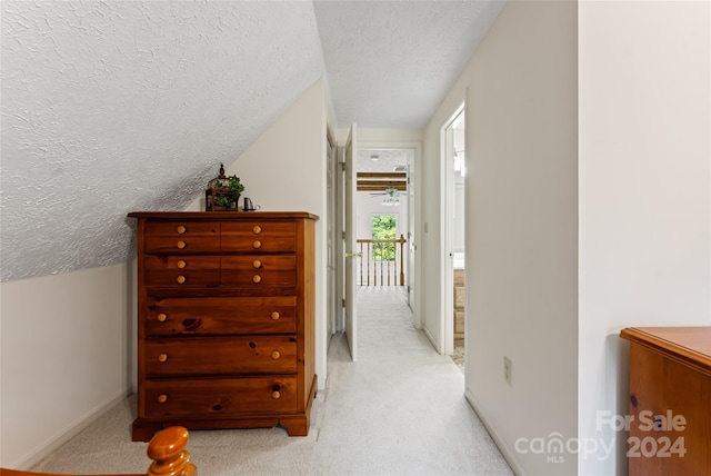 hall with a textured ceiling, vaulted ceiling, and light carpet