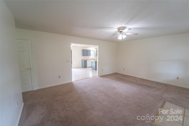 empty room featuring a textured ceiling, carpet, a ceiling fan, and baseboards