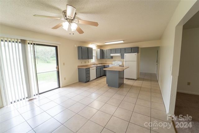 kitchen featuring gray cabinets, a kitchen island, a textured ceiling, white appliances, and under cabinet range hood