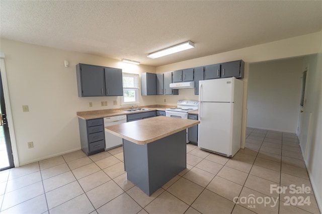 kitchen featuring white appliances, light countertops, under cabinet range hood, a sink, and light tile patterned flooring