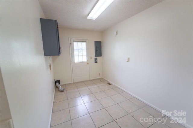 doorway with light tile patterned floors, a textured ceiling, electric panel, and baseboards