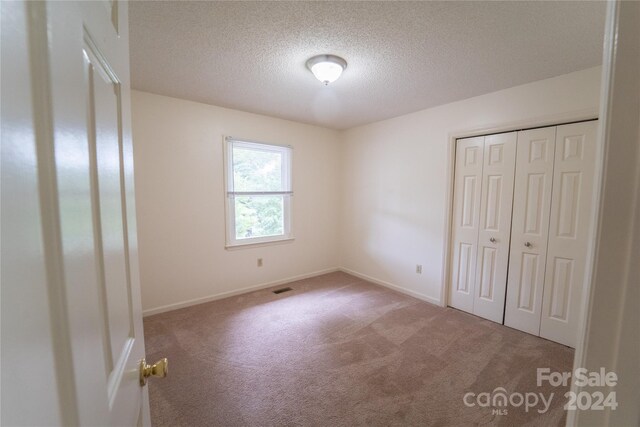 unfurnished bedroom featuring a closet, visible vents, carpet flooring, a textured ceiling, and baseboards