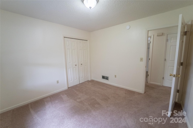 unfurnished bedroom featuring baseboards, visible vents, a textured ceiling, carpet floors, and a closet