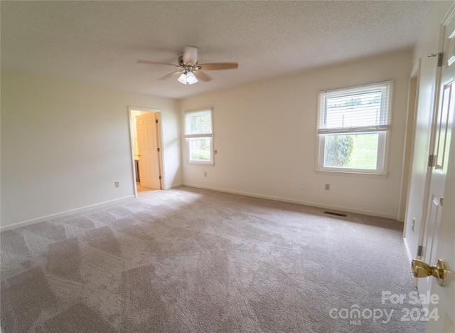 carpeted empty room featuring a textured ceiling, visible vents, a ceiling fan, and baseboards