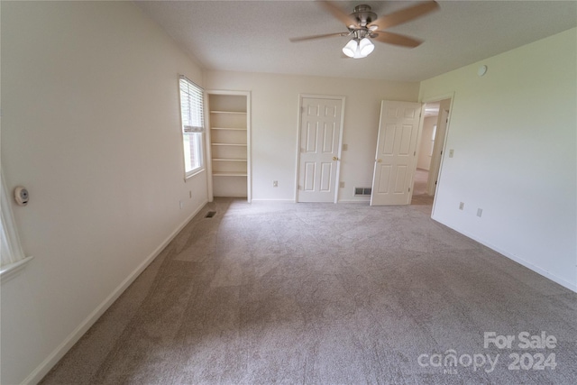 unfurnished bedroom featuring carpet flooring, a ceiling fan, visible vents, baseboards, and two closets