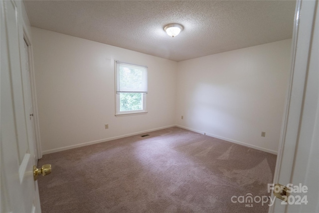 empty room featuring carpet floors, visible vents, baseboards, and a textured ceiling