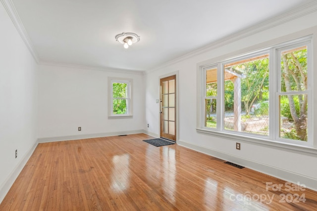 empty room featuring light wood-style floors, visible vents, crown molding, and baseboards