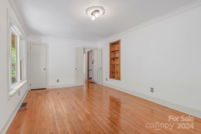 empty room featuring baseboards, visible vents, crown molding, and light wood finished floors