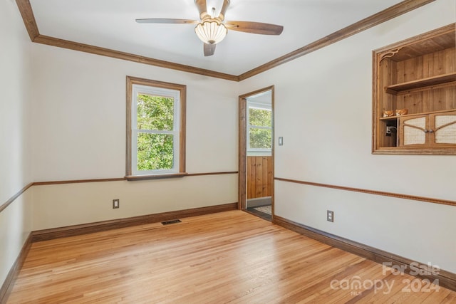 empty room featuring ornamental molding, light wood-style flooring, visible vents, and baseboards