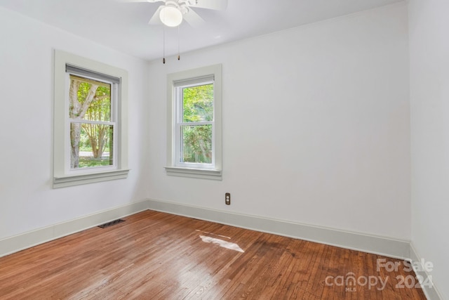 unfurnished room featuring a wealth of natural light, visible vents, baseboards, and hardwood / wood-style flooring