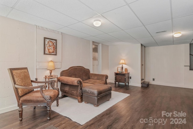 living area with a paneled ceiling, wood finished floors, visible vents, and baseboards