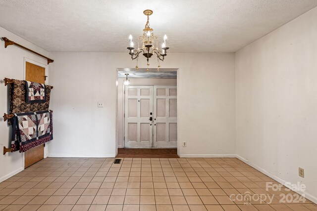 tiled spare room featuring a textured ceiling and a notable chandelier