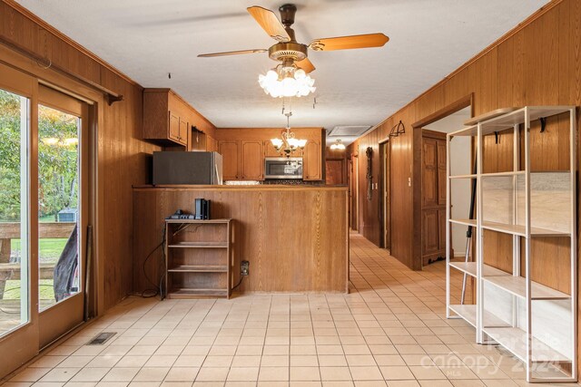 kitchen with ceiling fan with notable chandelier, appliances with stainless steel finishes, kitchen peninsula, and wooden walls